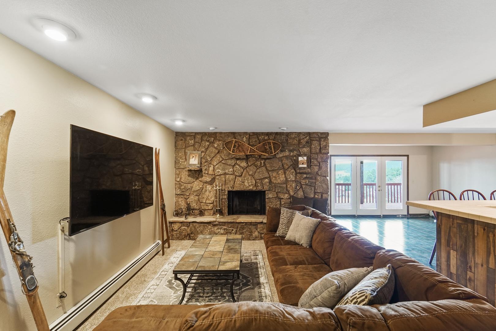 Basement TV room with stone fireplace, sectional sofa, and deck access